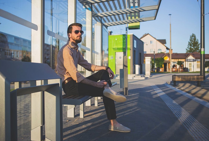 Homme barbu assis sur un banc à un arrêt de bus