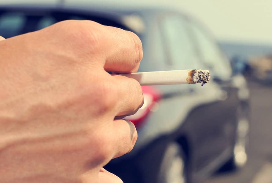 main qui tient une cigarette devant une voiture