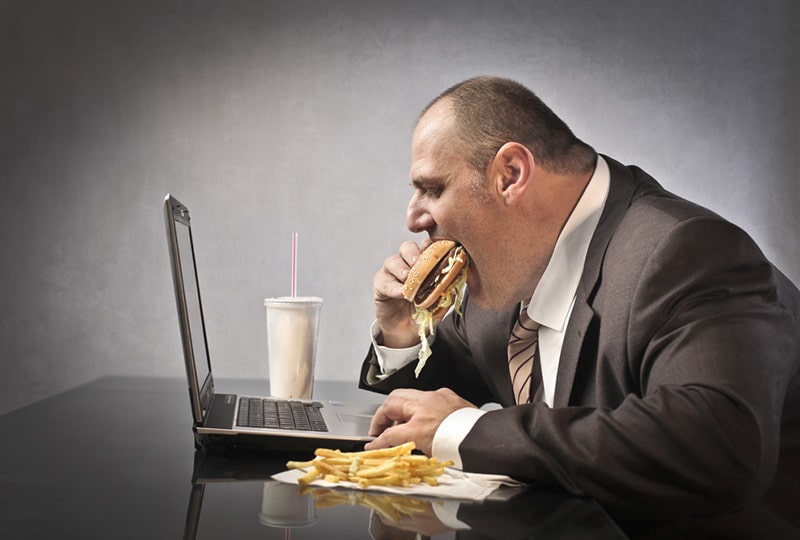 Homme obèse qui mange un sandwich au-dessus de son ordinateur
